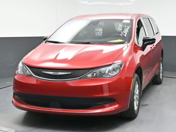 Front 3/4 view of a red minivan (Chrysler) indoors, front grille and headlights visible, driver-side window.