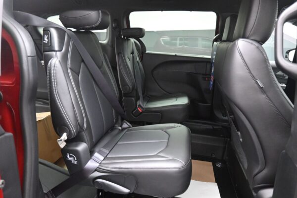 Two black leather captain chairs with white stitching in a vehicle's rear cabin, with seatbelts fastened.
