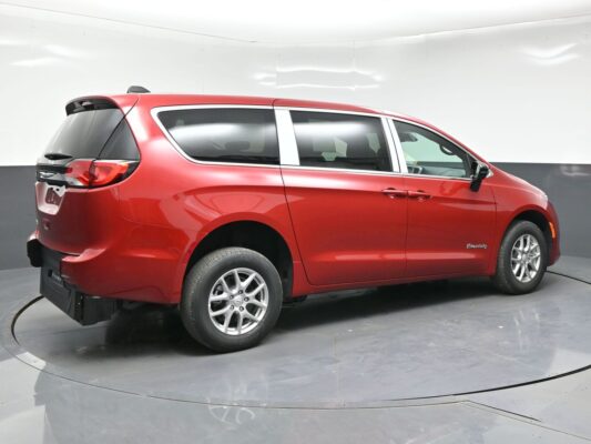 Red Chrysler Pacifica Hybrid minivan photographed in a studio on a rotating turntable, showcasing the side and rear profile with tinted windows and alloy wheels.