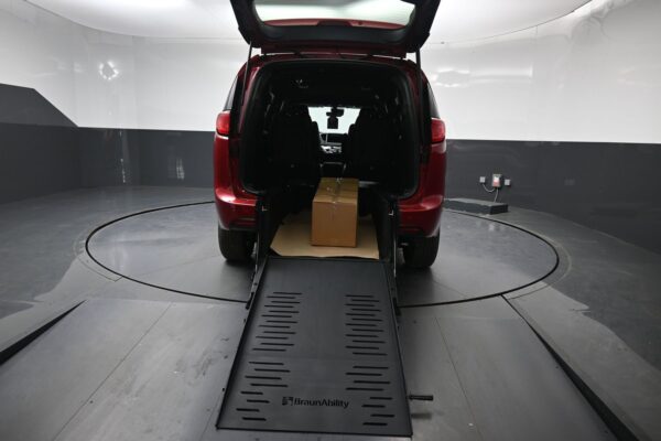Red SUV with rear hatch up and a wheelchair ramp extended to the ground, a cardboard box resting on the ramp inside the cargo area.