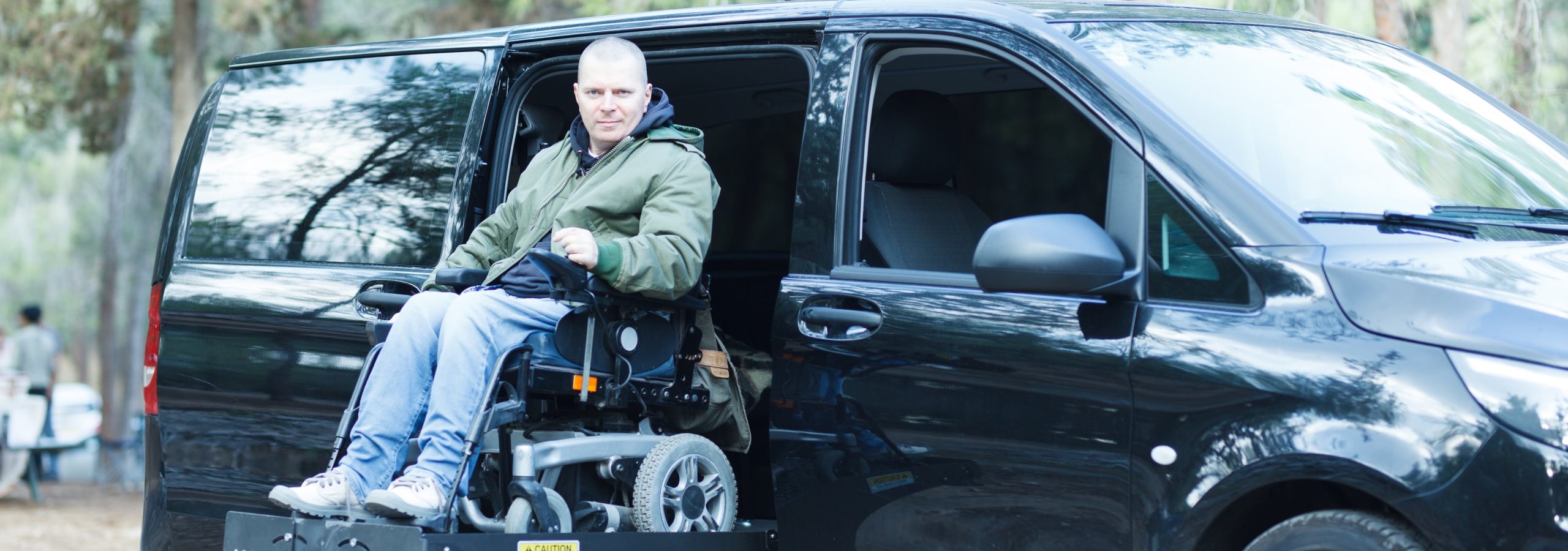 Disabled man on wheelchair on the car lift of an accessible passenger vehicle.