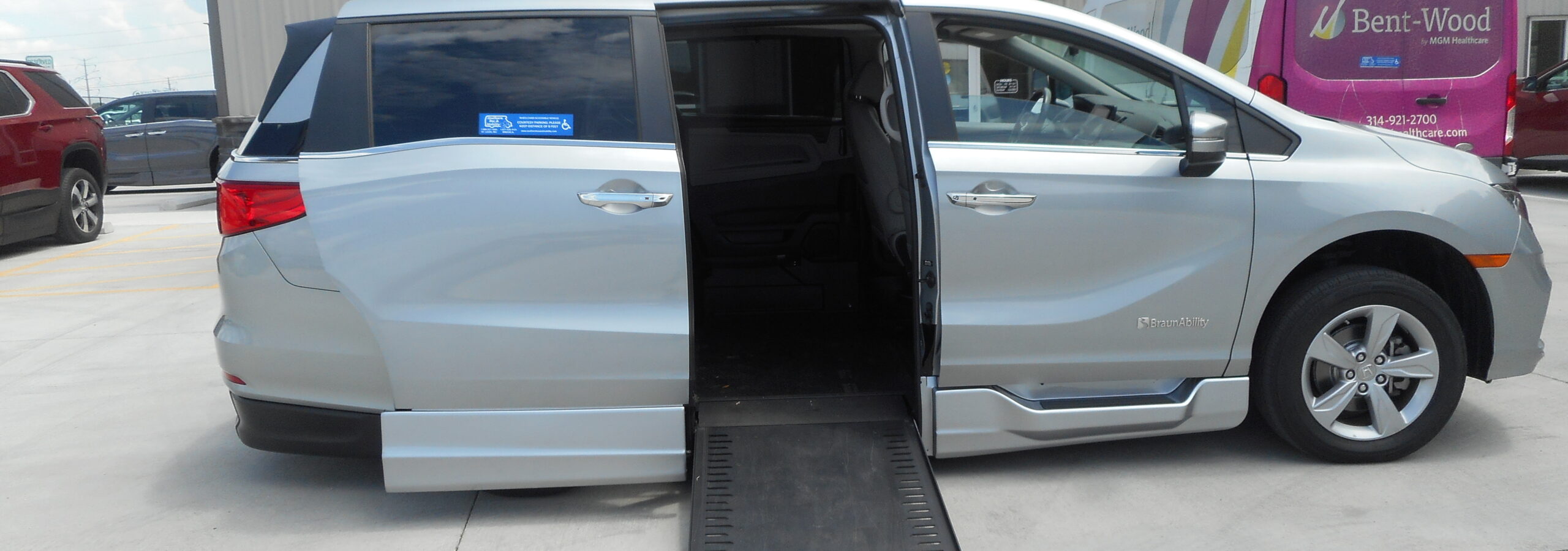 Silver minivan with a deployable wheelchair ramp extended in a parking lot in front of a mobility store sign reading 'Southern Bus & Mobility'