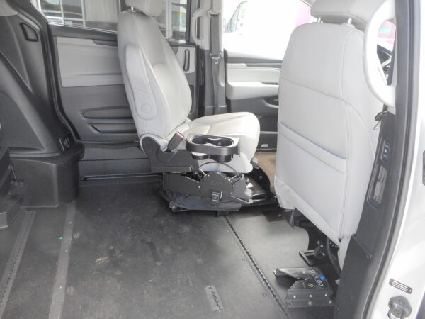 DSCN0024 Interior of a vehicle showing a mounted wheelchair lift/seat base and gray passenger seats, with space on the floor for mobility devices