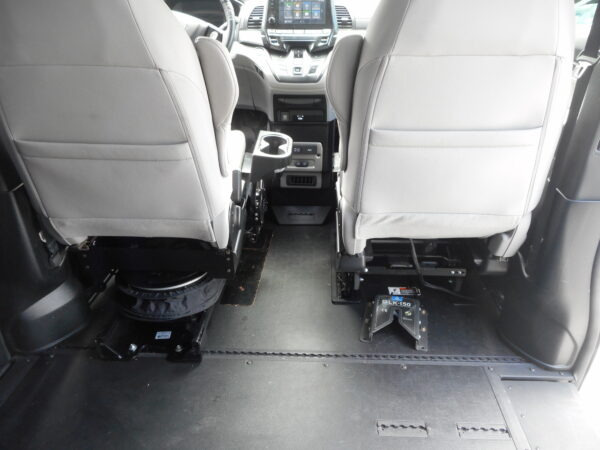 DSCN0025 Interior of a vehicle showing the backs of the front seats, center console, and floor-mounted equipment rails or base for a lift/attachment system at the rear area.