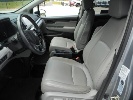 Interior of a gray car showing the steering wheel, driver and front passenger seats, and center console from the open door side