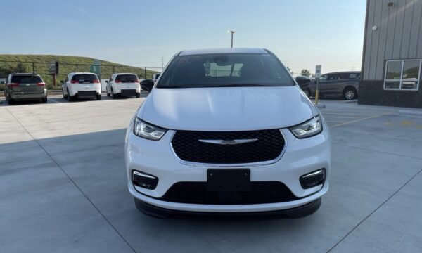 IMG_0395 Front view of a white Chrysler SUV facing the camera in a sunny dealership parking lot, with other cars in the background and a building to the right.