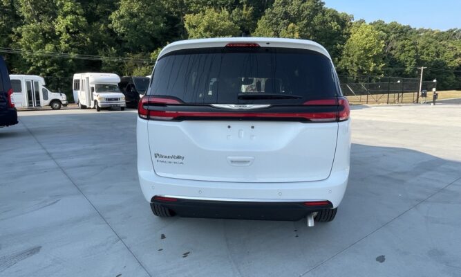 Rear view of a white BraunAbility Pacifica minivan in a parking lot, with red taillights and a large tinted rear window.
