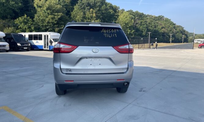 Rear view of a silver Toyota SUV parked in a lot, with other vans and a bus in the background and chalked numbers on the rear window.