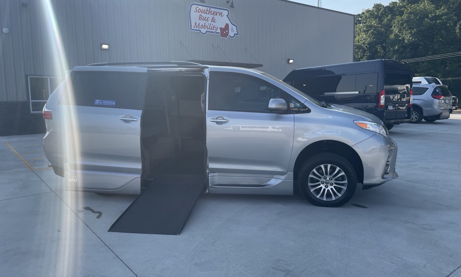 Silver minivan with a deployed side wheelchair ramp in a parking lot at a mobility-services facility (Southern Bus & Mobility)