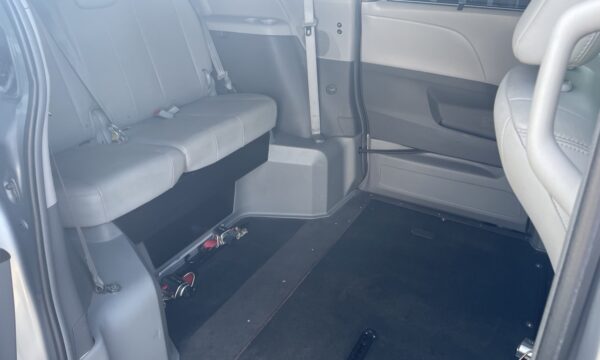 IMG_0408 Interior of a gray van with a rear bench seat and open floor space, showing tie-downs on the floor.