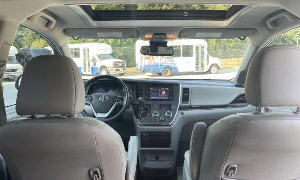 IMG_0410 Interior of a vehicle viewed from the back seats, showing the dashboard, steering wheel, center touchscreen, and sunroof; buses parked outside the windows.