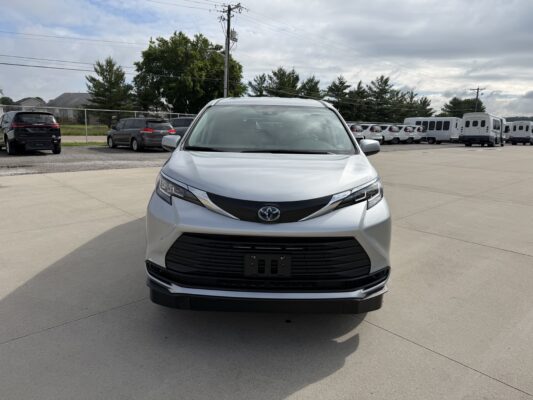Front view of a silver Toyota SUV in a parking lot with other cars and buses in the background, under a cloudy sky
