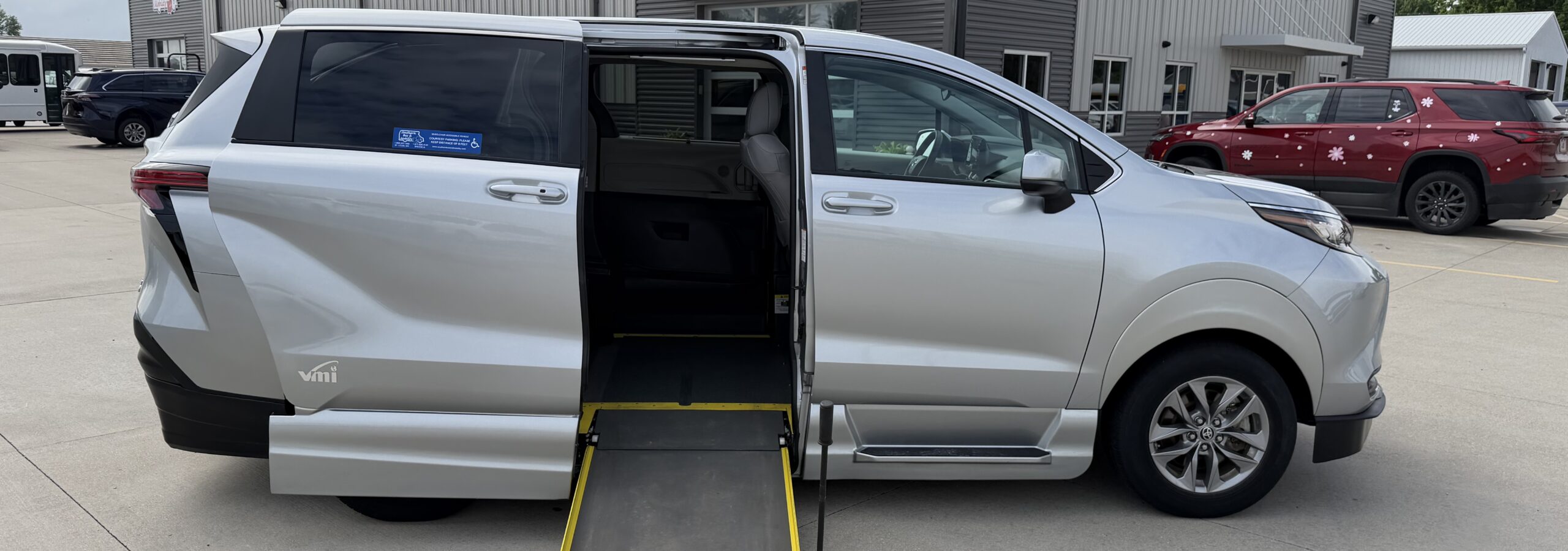 White SUV with the side-entry wheelchair ramp extended, parked in a lot outside a mobility services building.