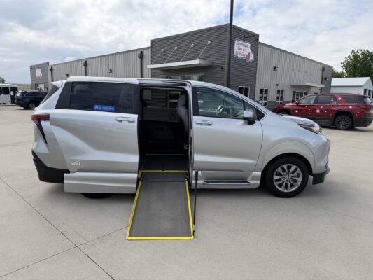 White SUV with the side-entry wheelchair ramp extended, parked in a lot outside a mobility services building.