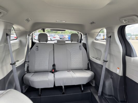 Rear interior of a gray minivan showing a folded third-row bench and two upright middle-row seats; parking lot visible through the windows.