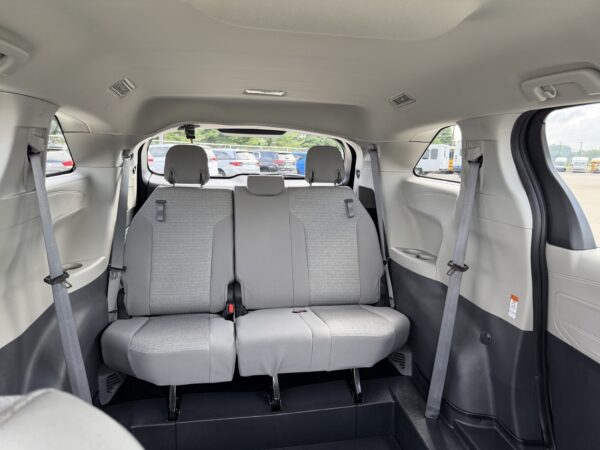 IMG_3384 Rear interior of a gray minivan showing a folded third-row bench and two upright middle-row seats; parking lot visible through the windows.