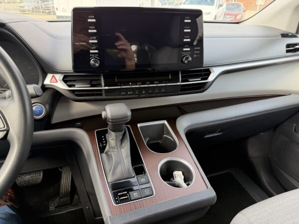 IMG_3387 Car interior: center touchscreen with control buttons, gear shifter, and cup holders across a woodgrain console area