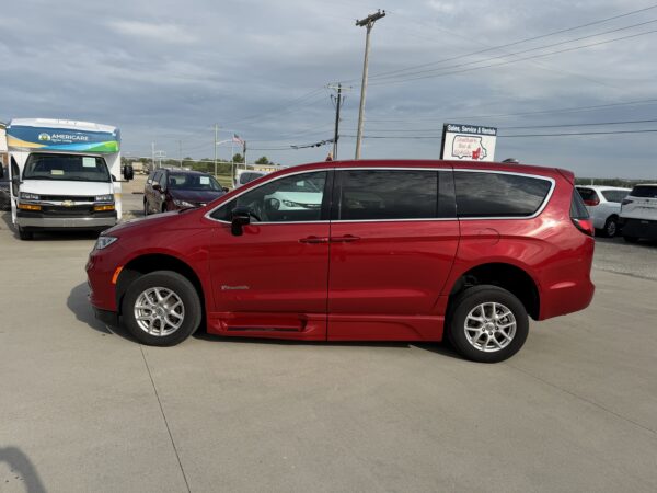IMG_3471 Red minivan in foreground at a car dealership lot; white Americare vehicle and dealership signs in the background.