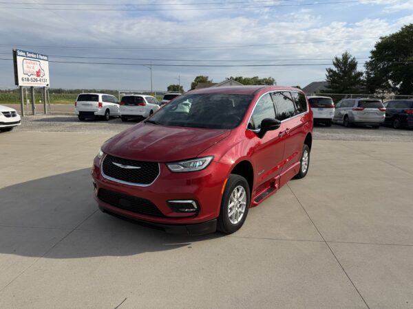 IMG_3472 Red minivan in the foreground at a dealership parking lot with white vans in the background and a Sales, Service & Rentals sign on the left.