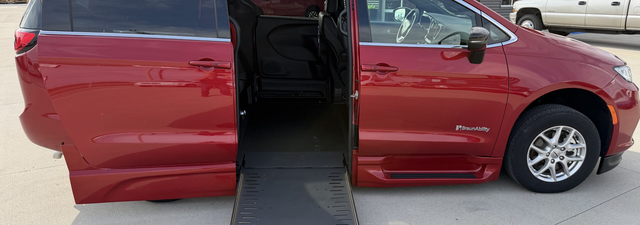 Red wheelchair-accessible van with a lowered ramp extending from side door at a dealership or service center.
