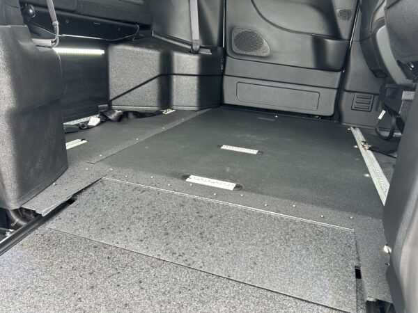 Empty cargo area of a vehicle with black carpet, side panels, and floor rails for securing cargo.