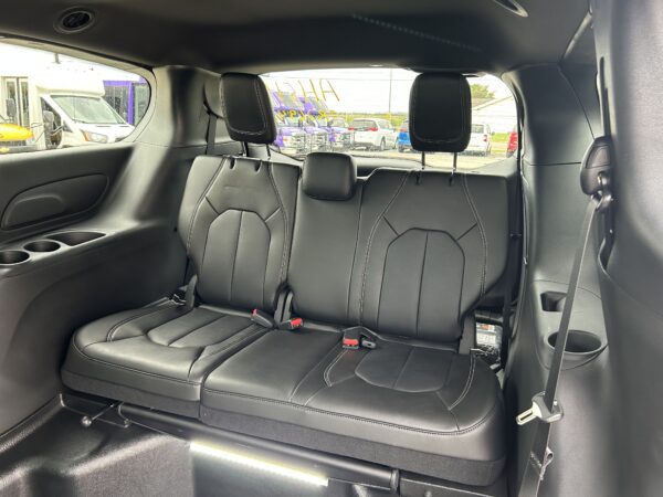 Rear seating area of a car with black leather seats, white stitching, and headrests visible through the window
