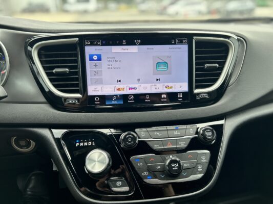 Car dashboard with a touchscreen infotainment system showing FM radio (SPORTS 101.1 MHz) and controls nearby