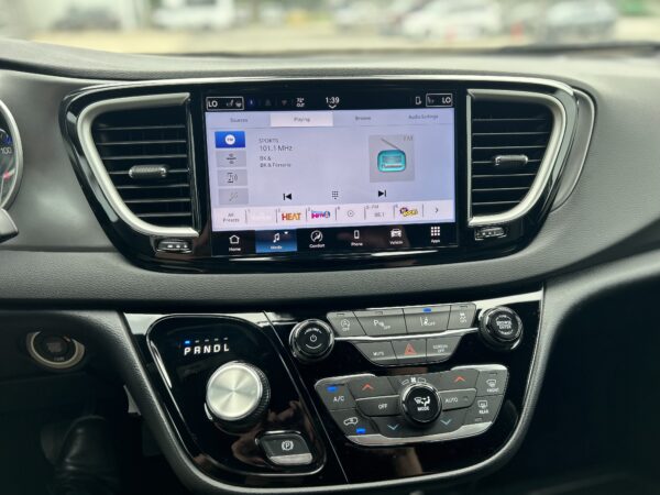 Car dashboard with a touchscreen infotainment system showing FM radio (SPORTS 101.1 MHz) and controls nearby