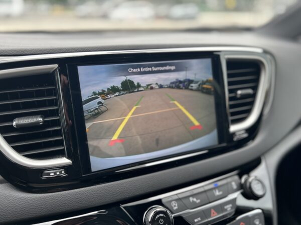 Car infotainment screen showing the rear‑view camera with parking guidelines in a parking lot.