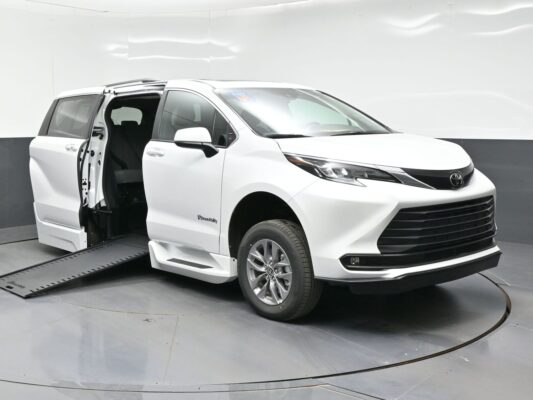 White Toyota minivan with a lowered side ramp extended for wheelchair access, doors open in a studio setting