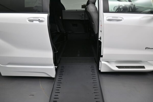 White accessible van with a side door open and a lowered ramp extending to the ground, ready for wheelchair access.