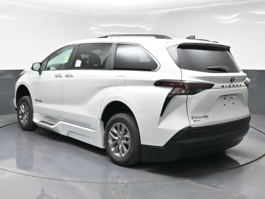 Rear three-quarter view of a white Toyota Sienna BraunAbility wheelchair-accessible minivan in a studio setting, showing side steps and tinted rear windows