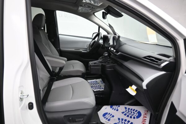 Interior of a white vehicle shown from the open driver’s side door, featuring gray front seats, center console, and steering wheel against a black dashboard. “