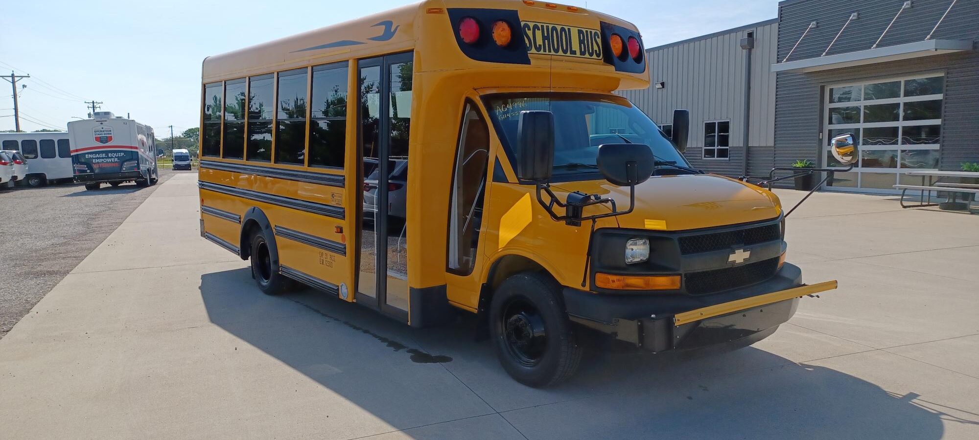 Yellow school bus parked in a lot beside a modern gray industrial building under a blue sky