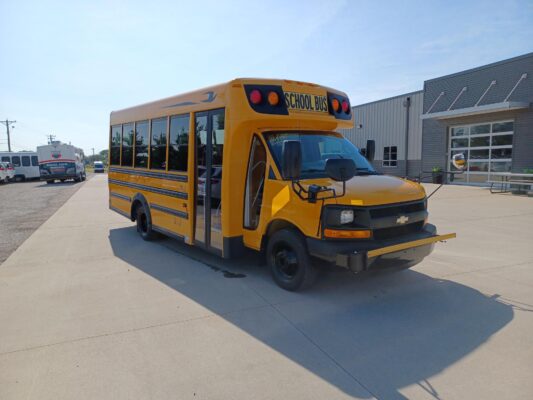Yellow school bus parked in a lot beside a modern gray industrial building under a blue sky