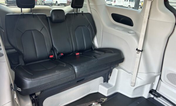 Three black leather seats in a vehicle's rear row with white stitching and visible seat belts