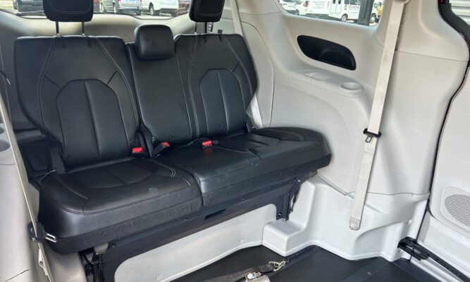 Three black leather seats in a vehicle's rear row with white stitching and visible seat belts