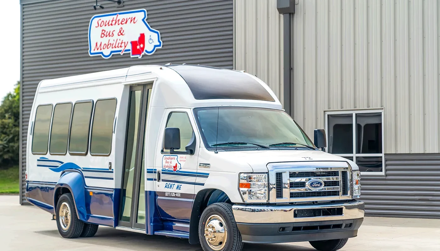 White and blue shuttle bus parked outside a gray metal building with a 'Southern Bus & Mobility' sign above it