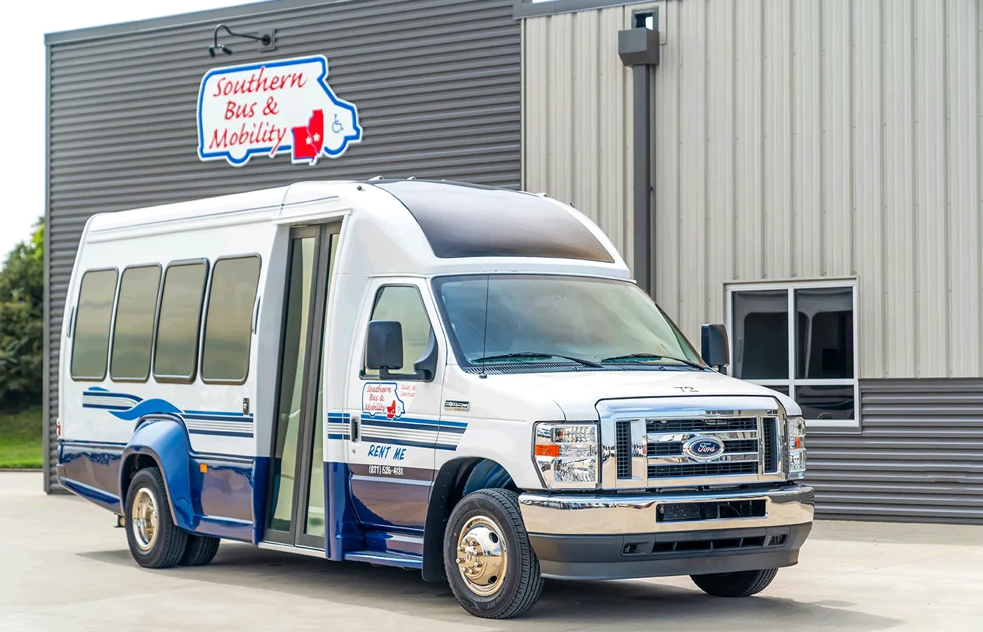 White and blue shuttle bus parked outside a gray metal building with a 'Southern Bus & Mobility' sign above it