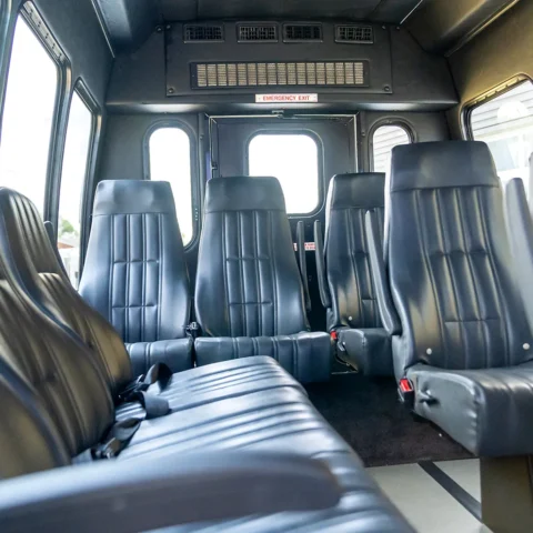 Interior of a small passenger bus with dark blue leather seats in rows, windows on both sides