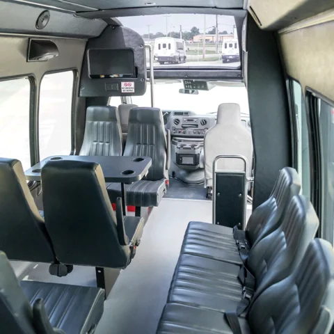 Interior of a passenger bus showing black leather seats, a small table with cup holders, and the view toward the driver’s area at the front of the cabin.