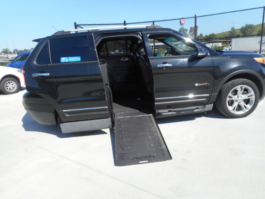 Black SUV with a deployed side-entry wheelchair ramp in a parking lot, ramp extending from the passenger side door.