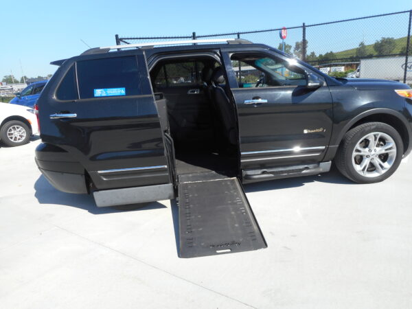 Black SUV with a deployed side-entry wheelchair ramp in a parking lot, ramp extending from the passenger side door.