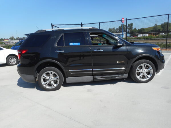 Black SUV with a wheelchair-accessible sticker on the rear window and a roof rack, parked in a lot next to a chain-link fence.