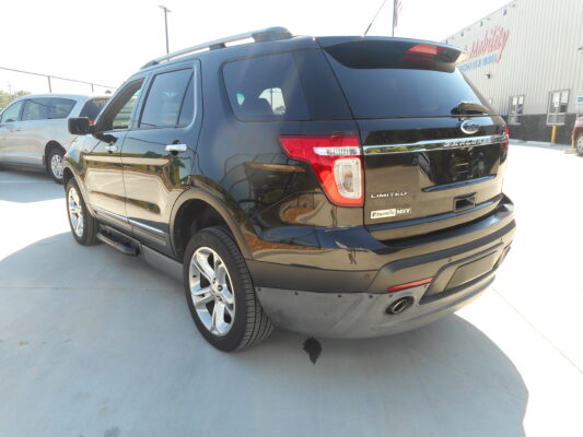 Black Ford Explorer Limited MXV SUV parked in a dealership lot beside a white minivan, with a mobility dealership building in the background.