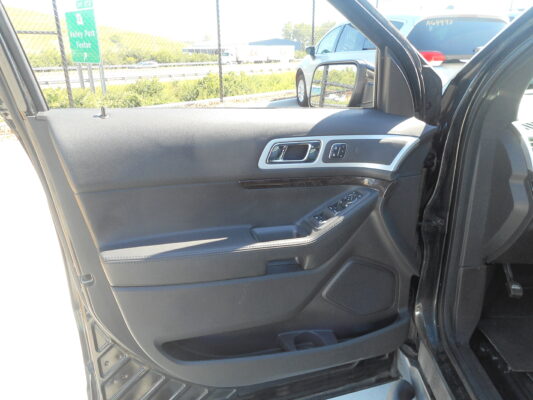 Interior of a car door panel featuring a silver door handle, black textured surface, and nearby power window controls on the armrest, with sunlight outside.