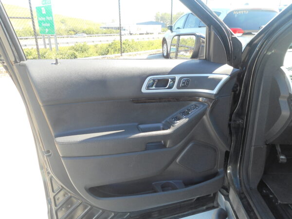 Interior of a car door panel featuring a silver door handle, black textured surface, and nearby power window controls on the armrest, with sunlight outside.