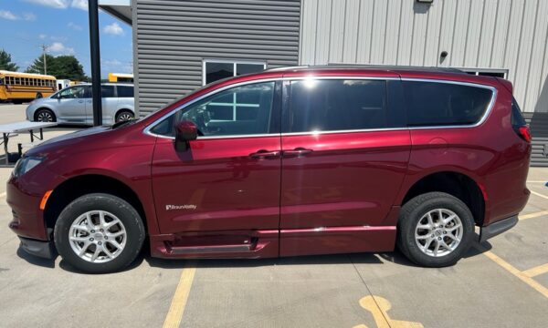 Maroon BraunAbility lowered-floor minivan with side entry, parked in a lot beside a gray metal building (tinted windows) in bright daylight.