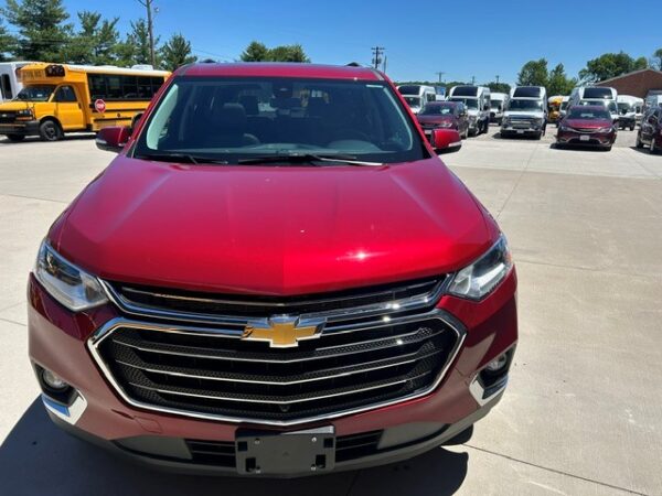 Red Chevrolet SUV front view in a parking lot with other vehicles and yellow school buses in the background