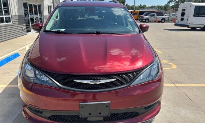 Front view of a maroon Chrysler SUV parked in a dealership lot, with a building and bus visible in the background.